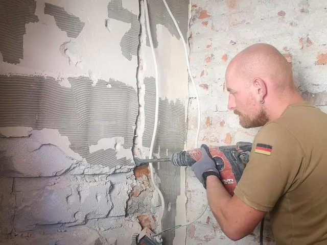 Elektriker stemmt mit dem Bohrhammer einen Schlitz für eine neue Leitung in eine alte Ziegelwand