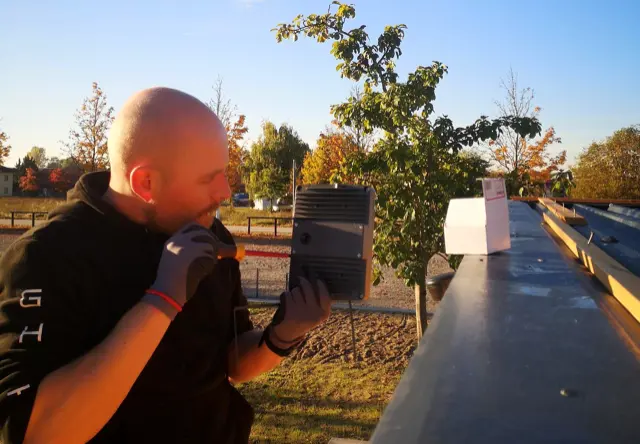 Monteur montiert eine Außenleuchte an einer Fassade, im Hintergrund herbstliche Bäume