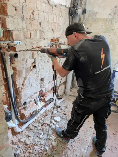 Monteur stemmt mit dem Bohrhammer einen Schlitz in eine alte Ziegelwand