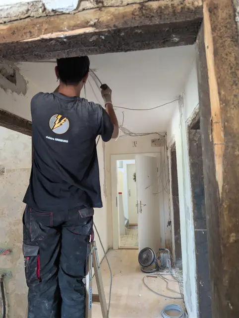 Monteur zieht im entkernten Flur eine neue Leitung unter der Holzbalkendecke ein