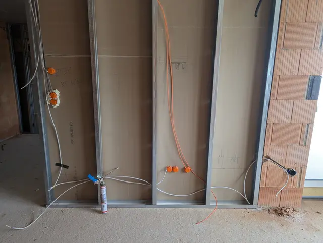 Rohinstallation im Ständerwerk mit orangen Verbindungsklemmen, rechts eine Ziegelwand