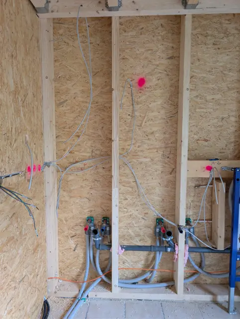 OSB-Wand mit Elektroleitungen, Dosen und Wasserleitungen, die Positionen sind markiert