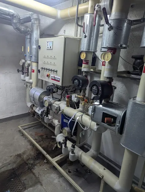 Technikraum mit Rohrleitungen, Pumpen und dem zugehörigen Schaltkasten an der Wand