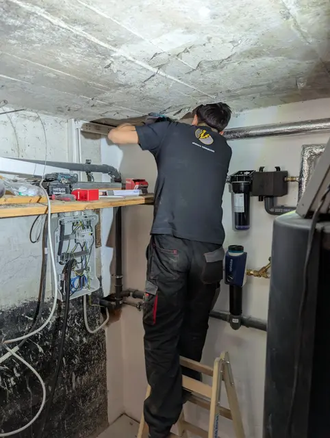 Monteur befestigt unter der Kellerdecke eine neue Leitungsführung